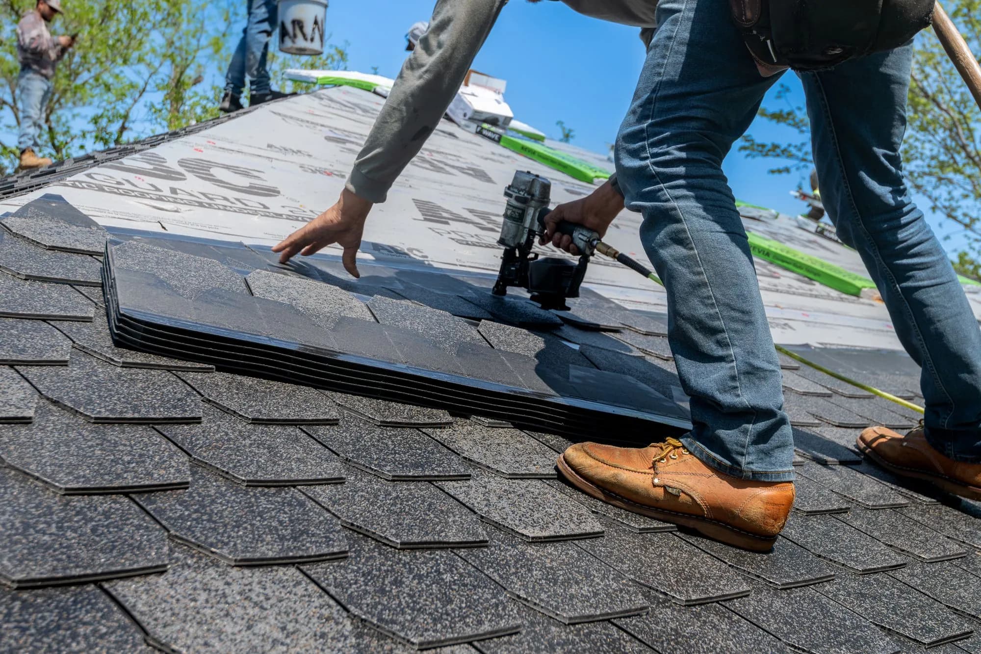 Roofer using a nail gun to install new asphalt shingles